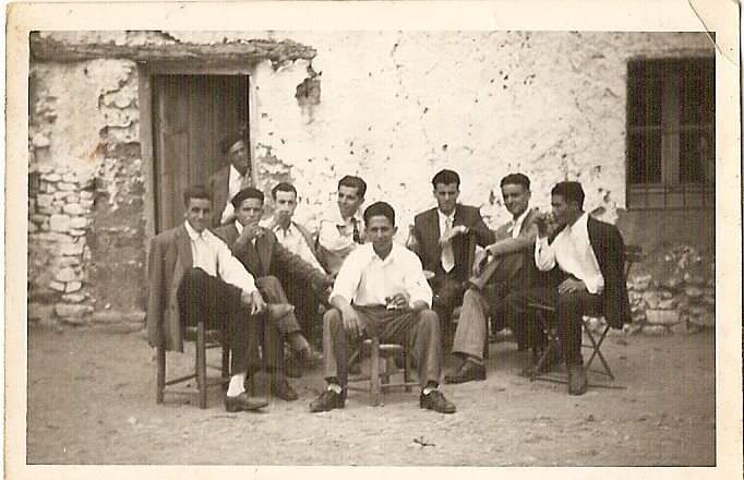 Fotografía B/N de un grupo de hombres bebiendo en la fachada de una casa rural